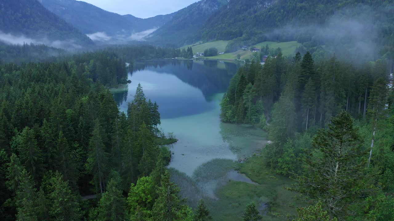 空中:森林中绿色树木上的云朵移动的风景，无人机在内陆湖上空下降视频素材