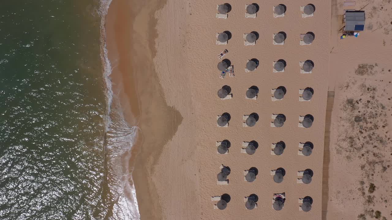 葡萄牙海滨度假胜地的鸟瞰图。阳伞和阳光躺椅从上到下安置在黄色的海滩上。阿尔加夫视频素材