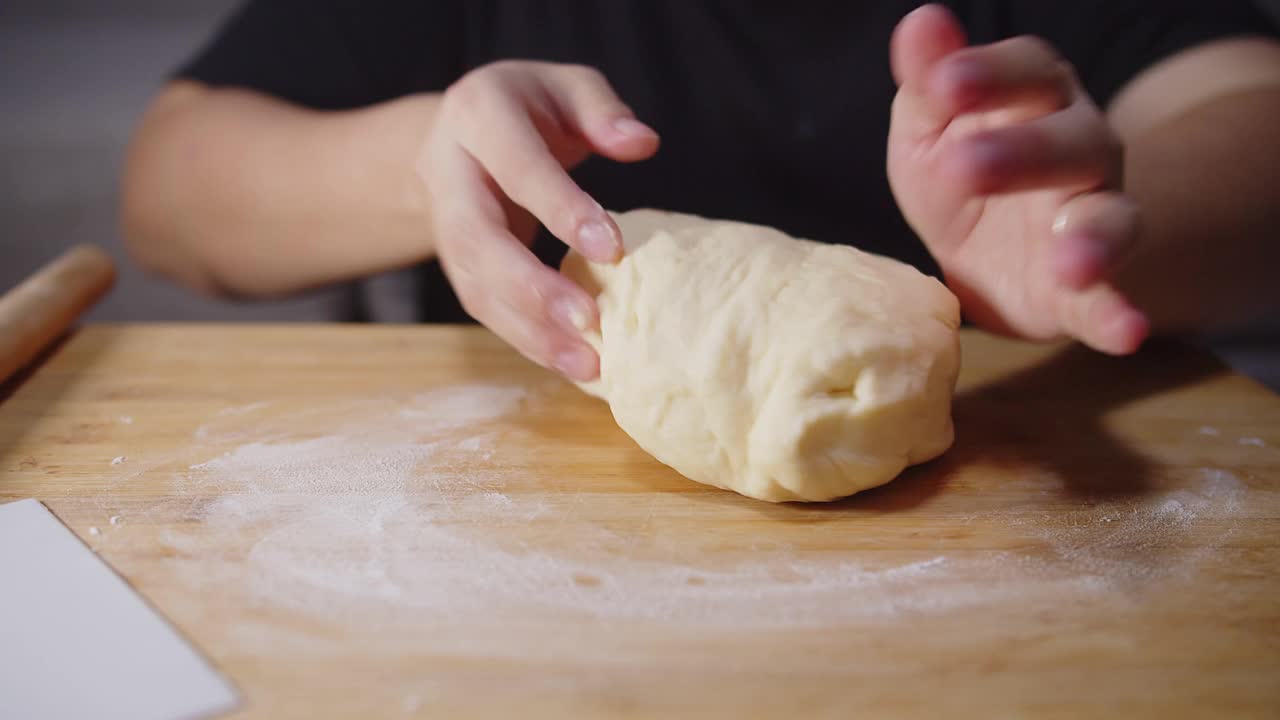 近面点师傅手握并在木板上切割自制的软面团，准备在厨房面点制作面包视频素材