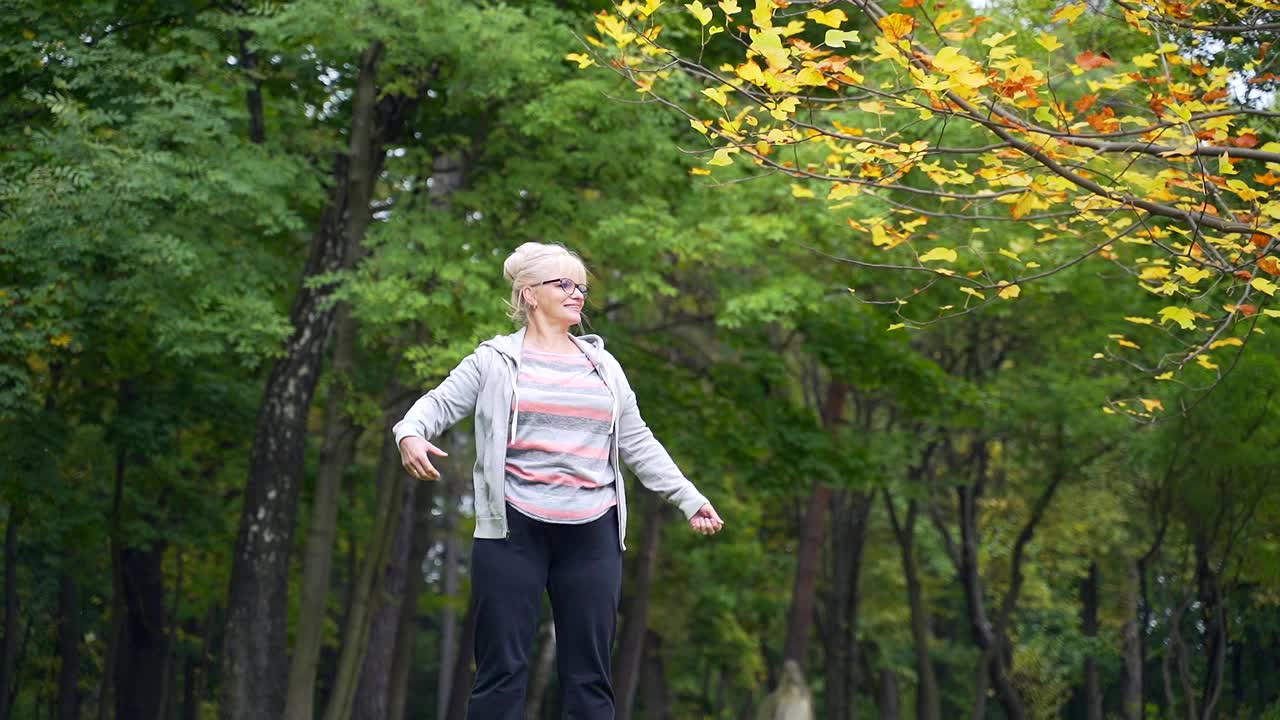 老年活跃女性在户外公园做健美操或体操运动。一位50多岁的退休妇女正在进行锻炼视频素材