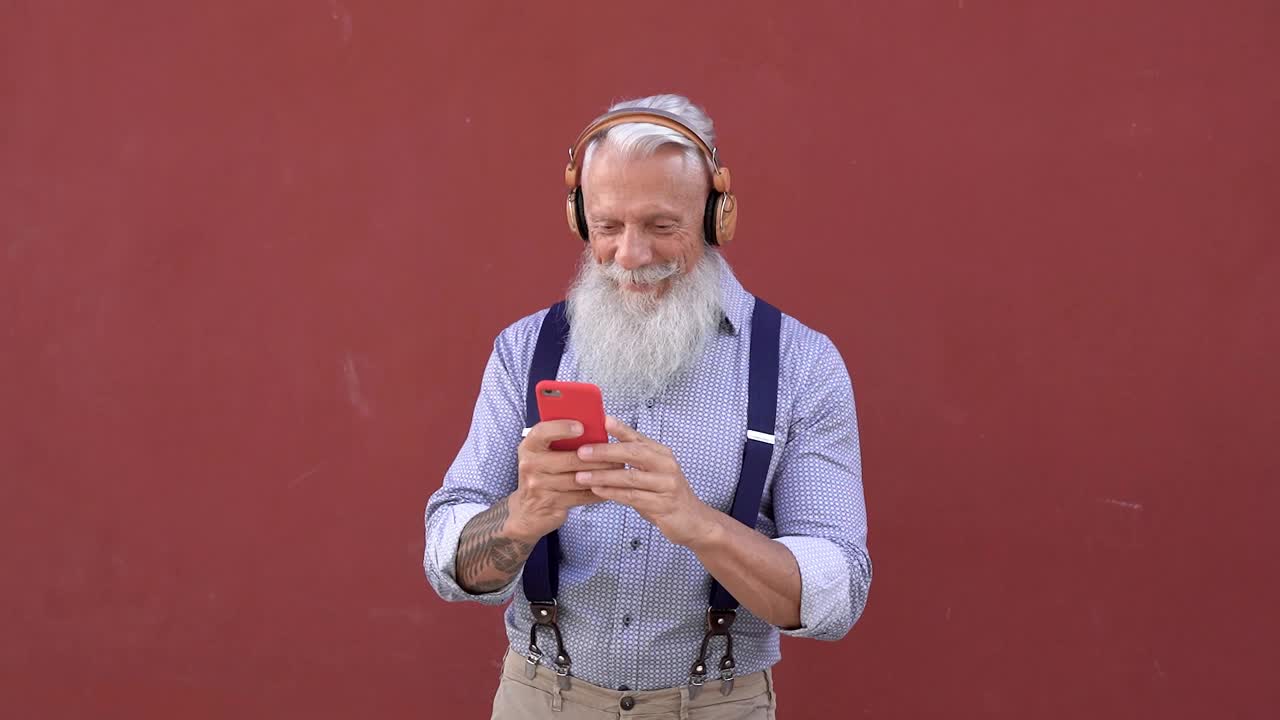 老年潮人使用手机和无线耳机听音乐-老年人享受技术趋势视频素材