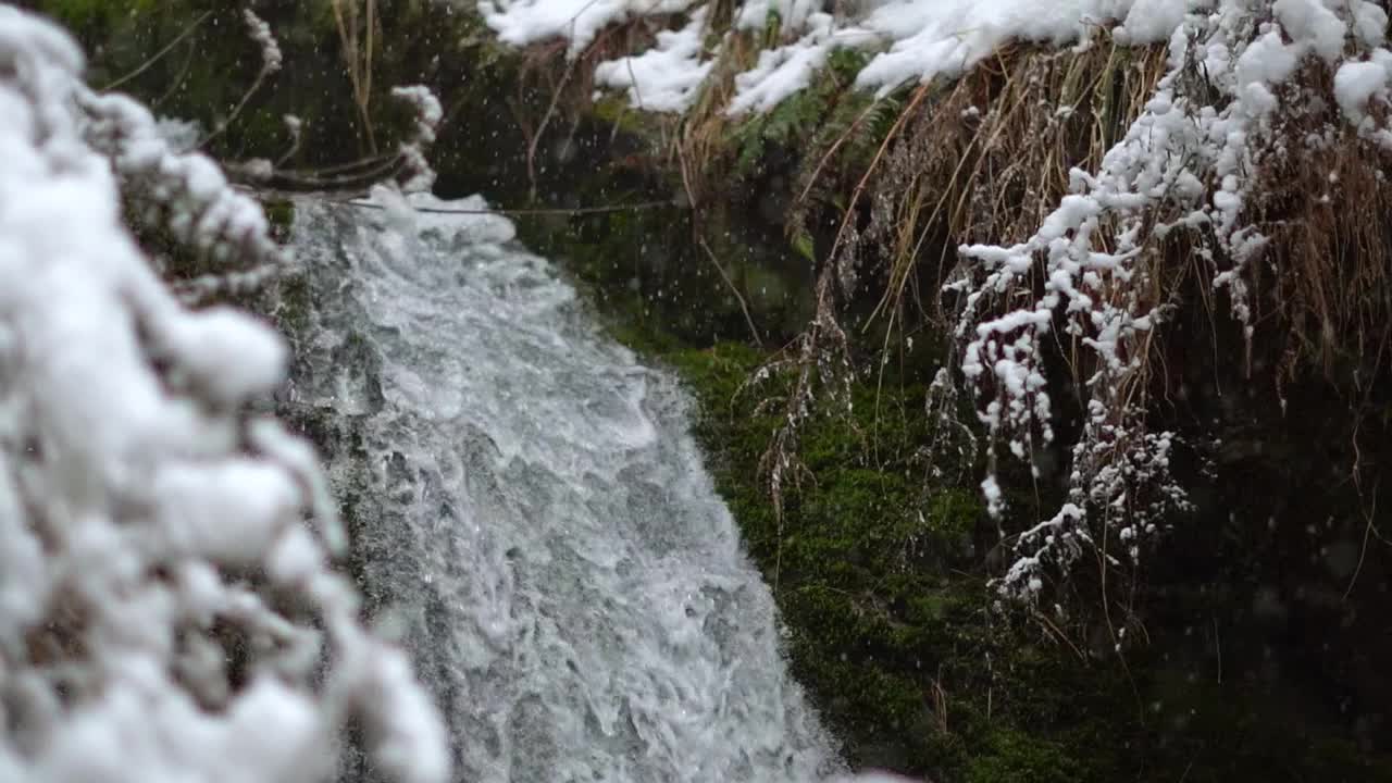 在印度喜马偕尔邦的库鲁，贾纳瀑布的水在冬天下雪时流动的慢动作镜头。下雪时瀑布的景色。冬天的背景。视频素材