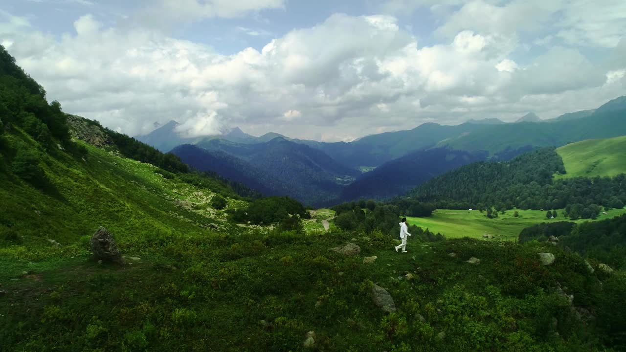 一名女登山者在山顶的航拍照片。镜头跟随穿着白色夹克的年轻潮女跑上山顶视频素材