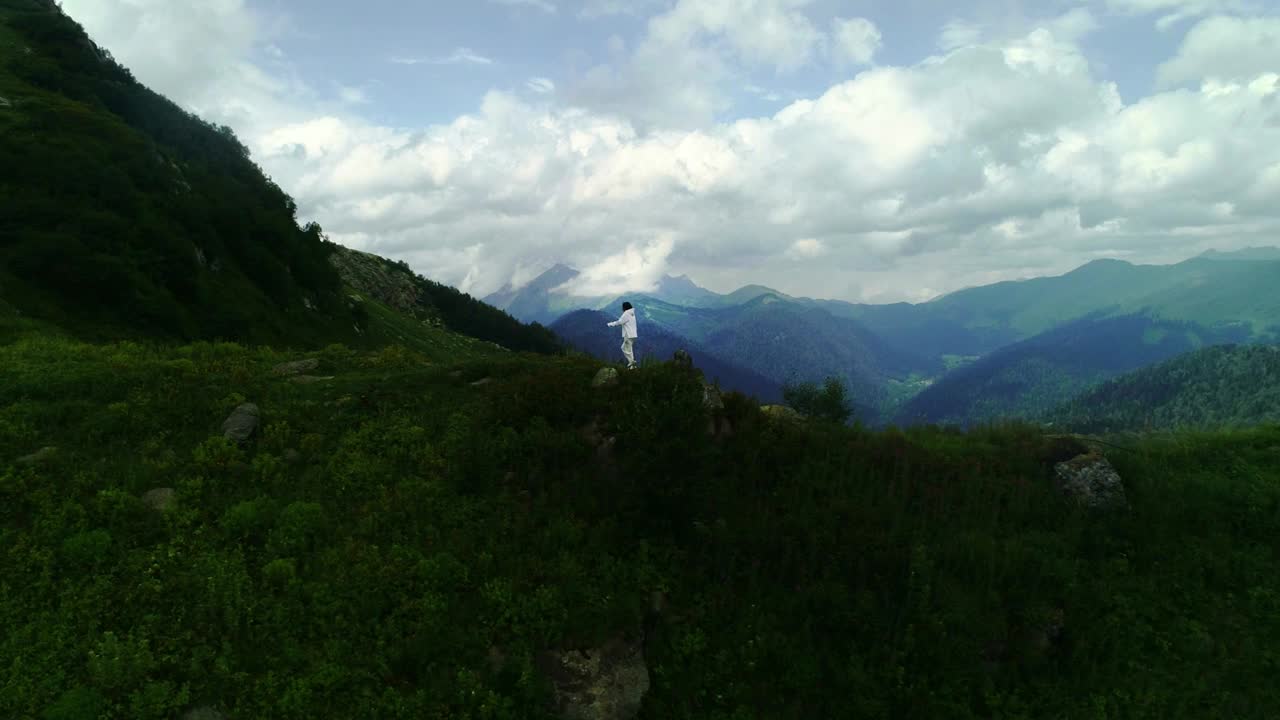 一名女登山者在山顶的航拍照片。镜头跟随穿着白色夹克的年轻潮女跑上山顶视频素材