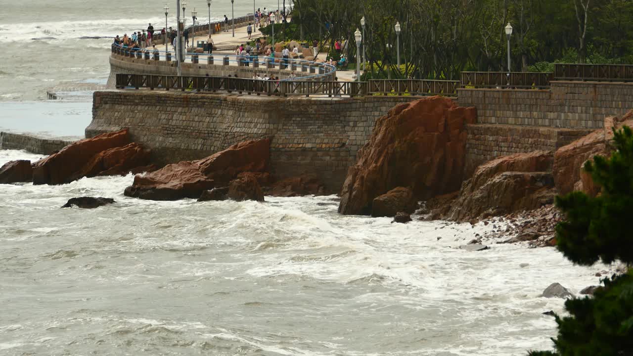 4k海浪冲过堤坝，人们上岸。海洋海水和海岸岩石浪涌海岸。视频素材