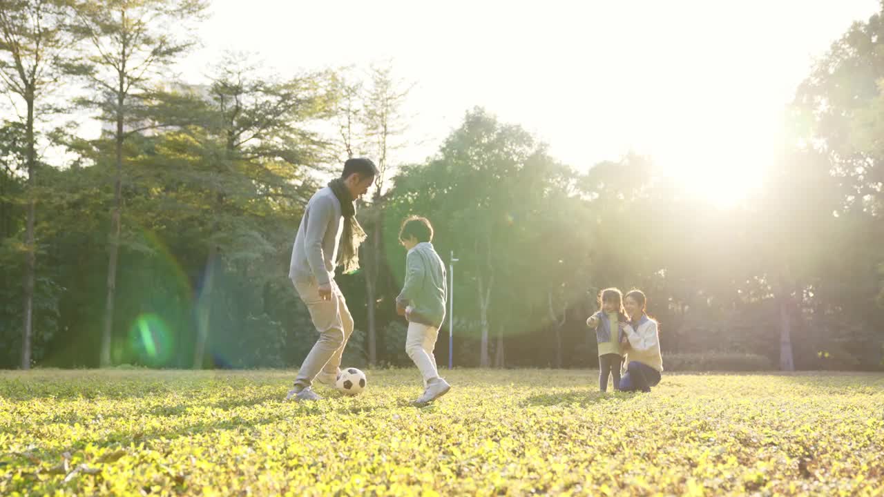 一个亚洲小男孩和爸爸在公园里踢足球视频素材