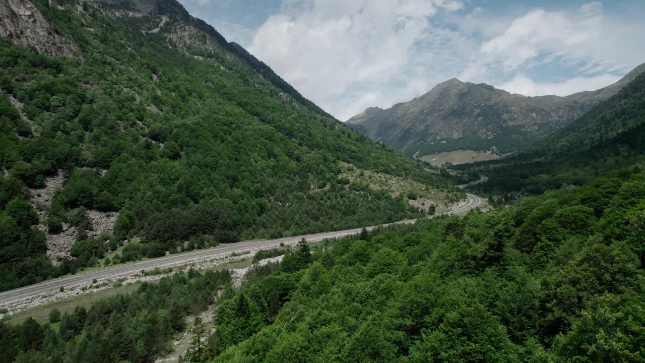 美丽的无人机视野的沥青公路在高山上。山脉消失在天空中，天空有些许阴云，但山峰被阳光照亮。视频素材