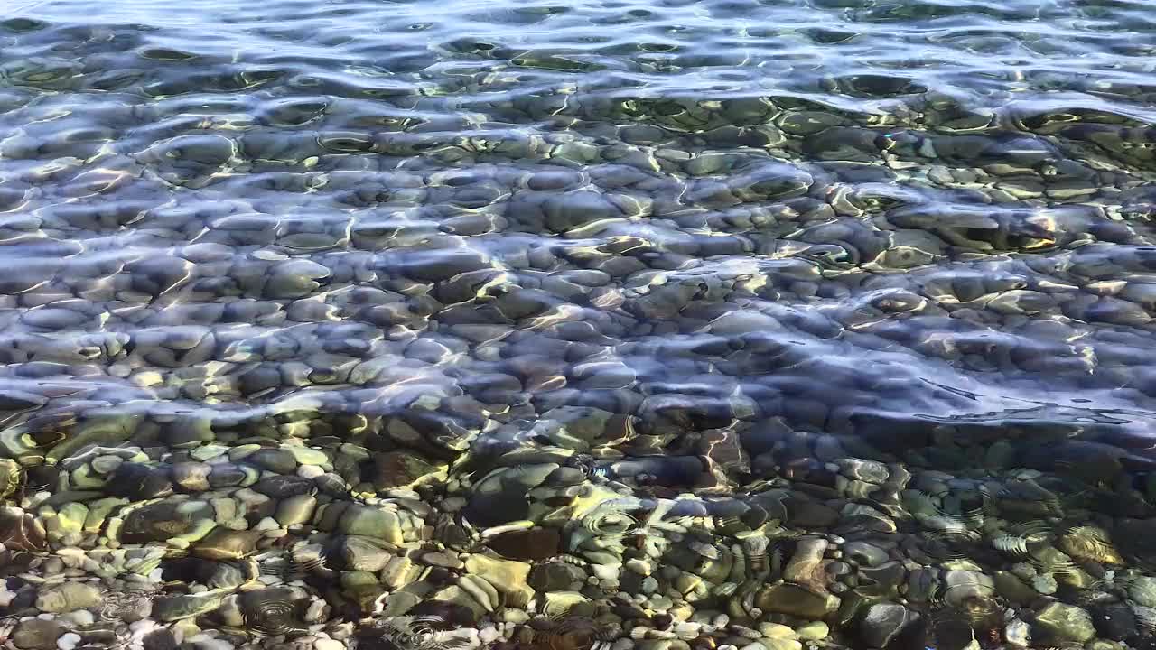 海卵石滩上有五颜六色的石头，透明的波浪没有泡沫，在一个阳光明媚的秋日视频素材