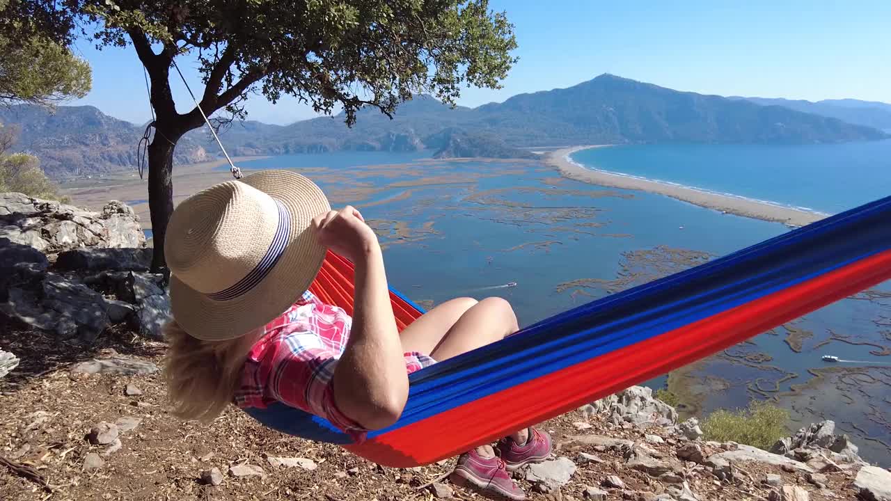 一个年轻漂亮的女人躺在吊床上看着大海。视频素材