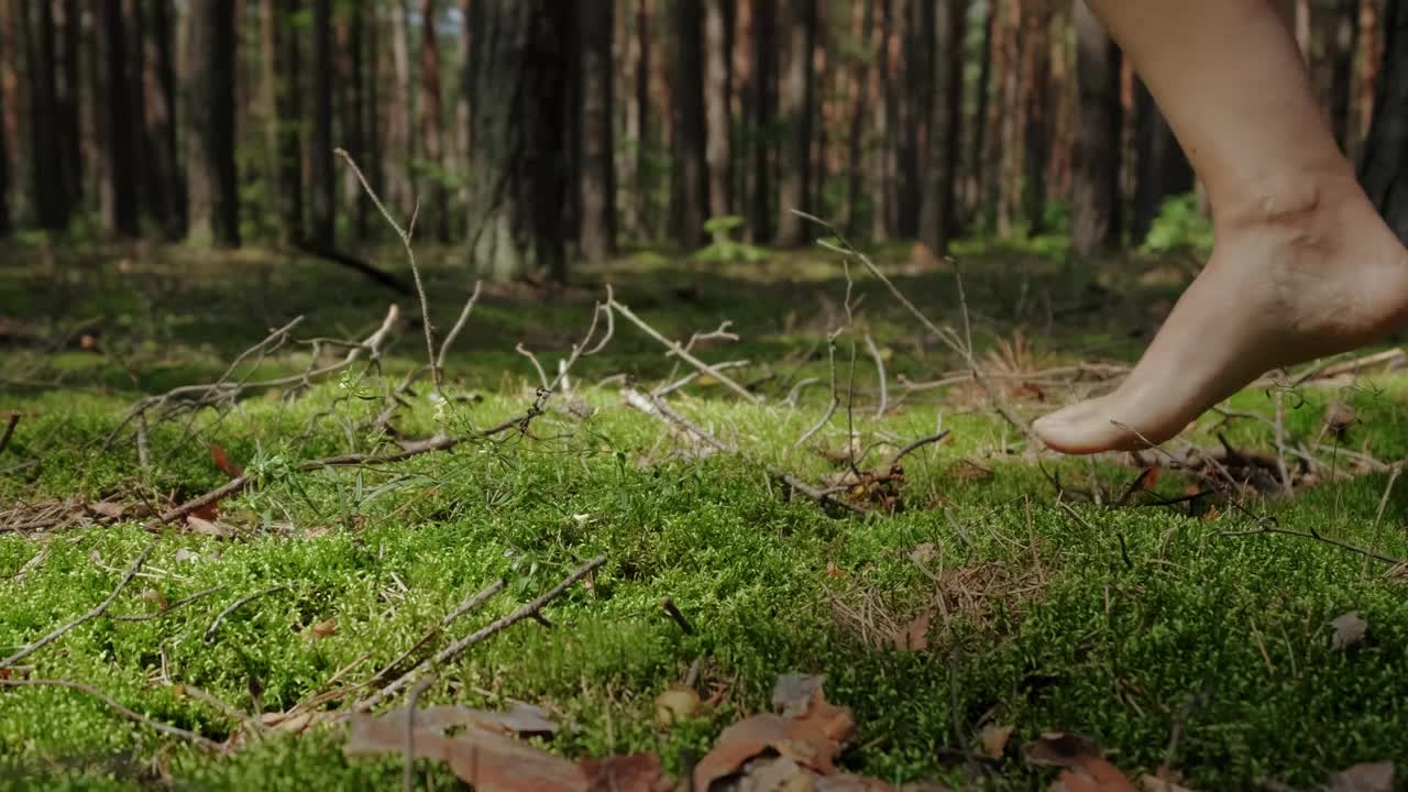 阳光明媚的日子里，一个女人赤脚走在森林里柔软的绿色苔藓上。视频素材