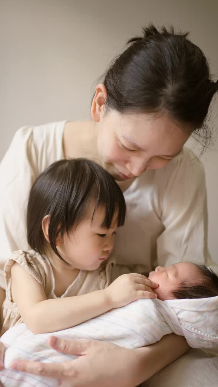 妈妈和妹妹在家里的卧室里照顾婴儿。视频素材