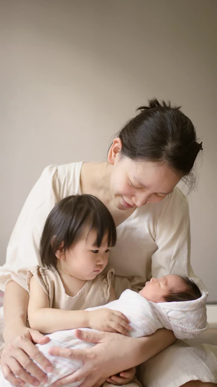 妈妈和妹妹在家里的卧室里照顾婴儿。视频素材