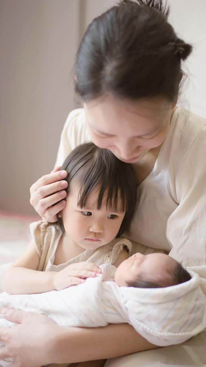 妈妈和妹妹在家里的卧室里照顾婴儿。视频素材