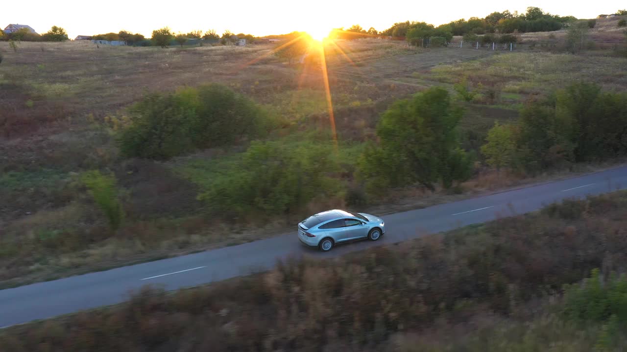 电动汽车在乡村道路上行驶的鸟瞰图，背景是明亮的日落。在乡村公路上快速行驶的现代车辆。电动环保汽车骑行。视频素材