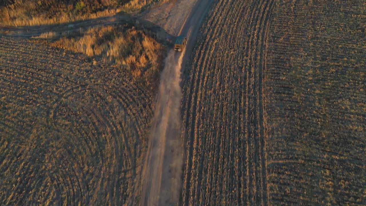 空中拍摄的农民吉普车行驶在空旷的乡村道路之间的田地。黄昏时分，在尘土飞扬的道路上超速行驶的车辆。在夏日，飞过乡间路上的汽车。俯视图视频素材