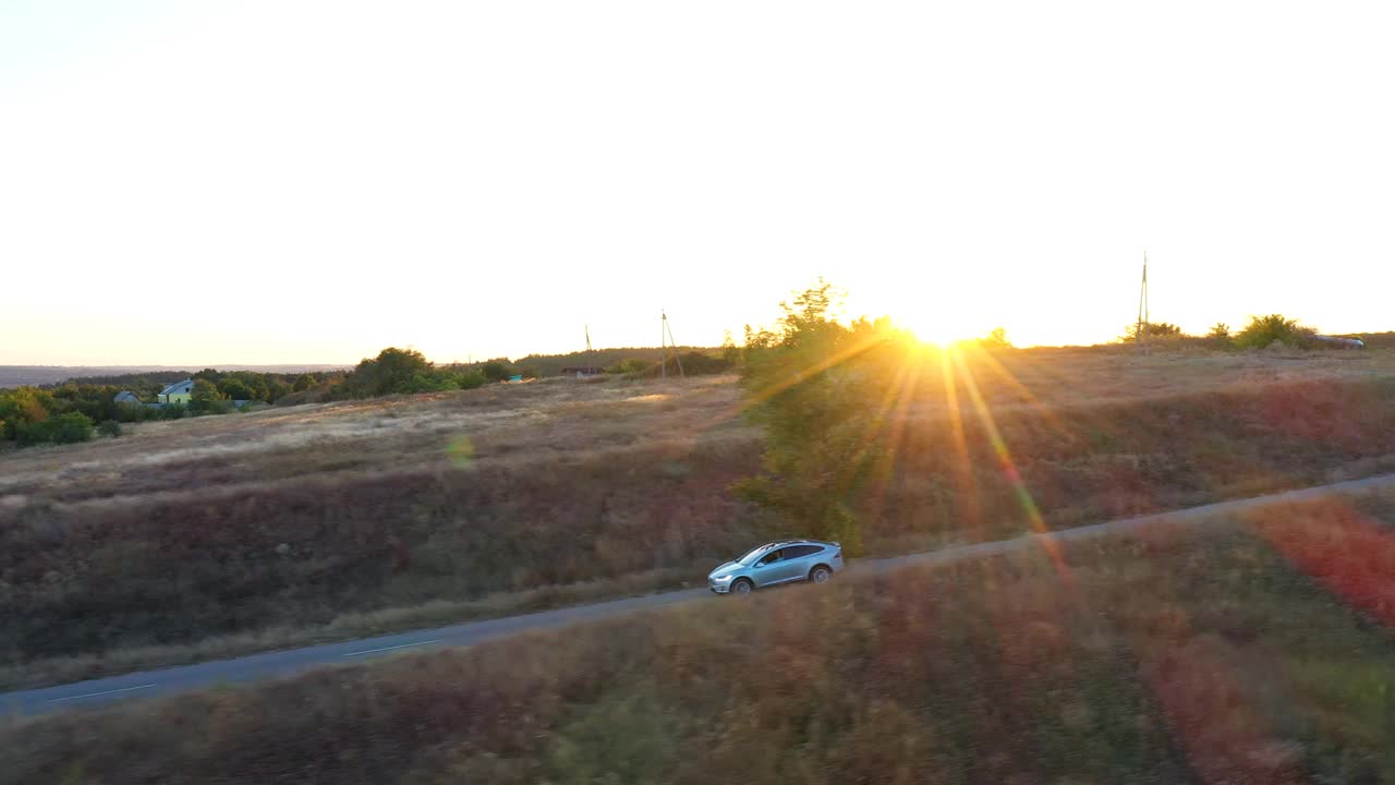 空中拍摄的电动汽车行驶在乡村道路与明亮的日落背景。在乡村公路上快速行驶的现代车辆。电动环保汽车骑行。侧视图视频素材