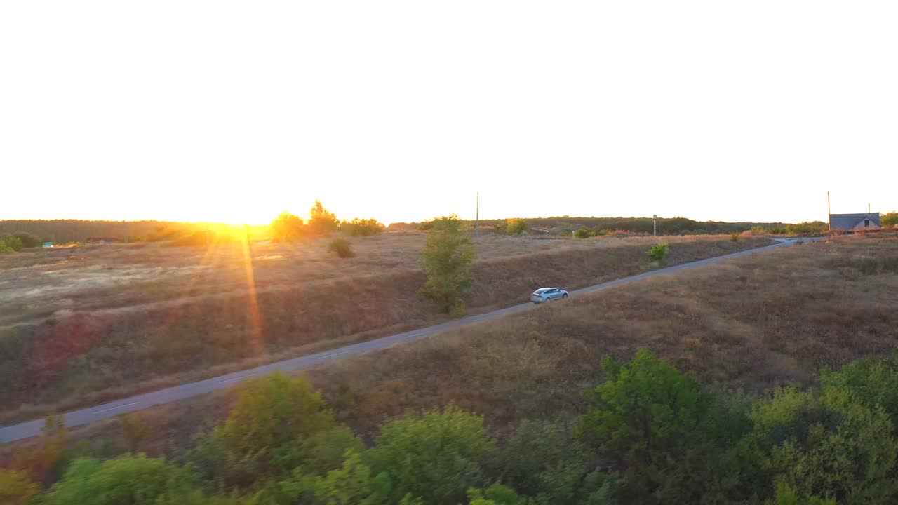 电动汽车在乡村道路上行驶的鸟瞰图，背景是明亮的日落。在乡村公路上快速行驶的现代车辆。电动环保汽车骑行。视频素材