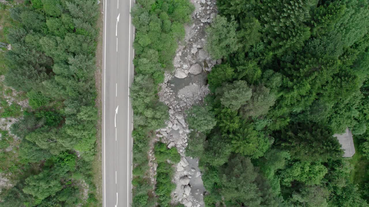 柏油路在一个山谷的高山。在它旁边，一条山间河流在树木之间蜿蜒流过。视频素材