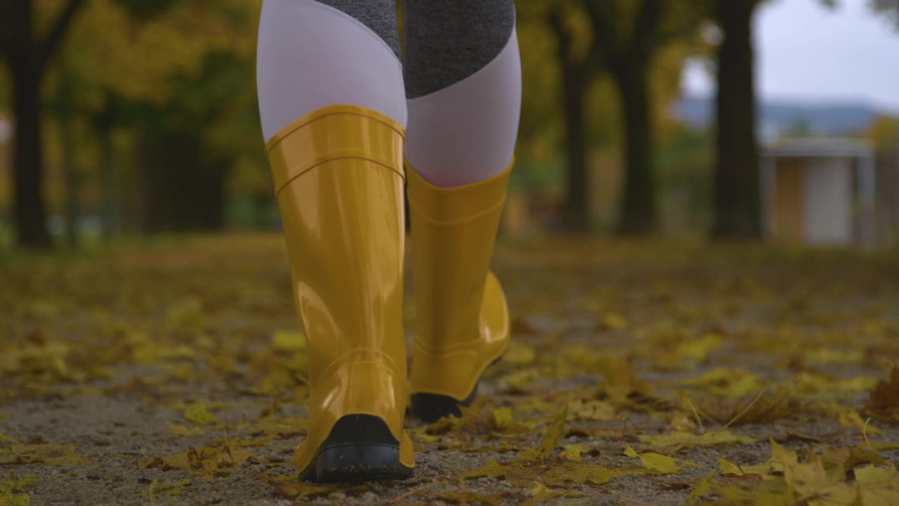 特写，DOF:穿着胶靴的女人走在树叶覆盖的大街上。视频素材
