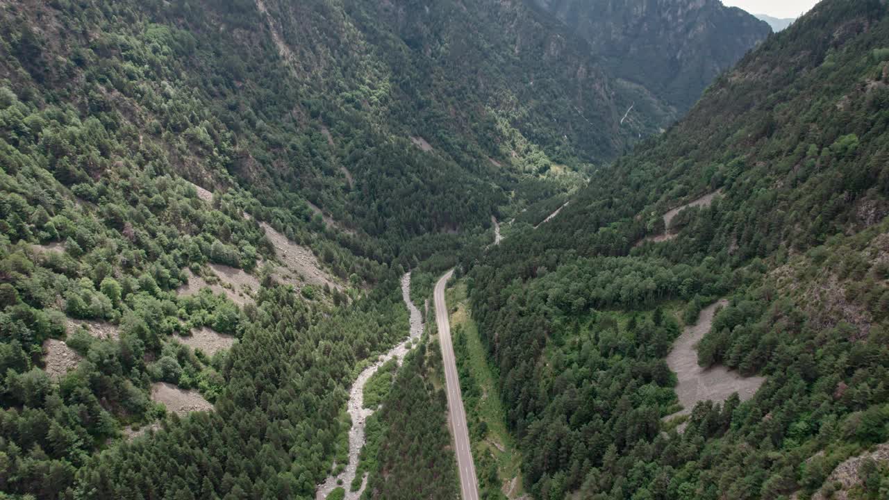 美丽的无人机视野的沥青公路在高山上。山脉消失在天空中，天空有些许阴云，但山峰被阳光照亮。视频素材