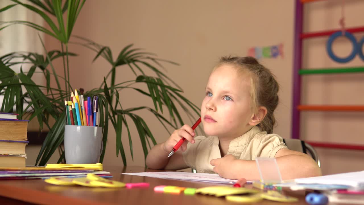 学龄前儿童坐在桌子旁思考。她做家庭作业。视频素材