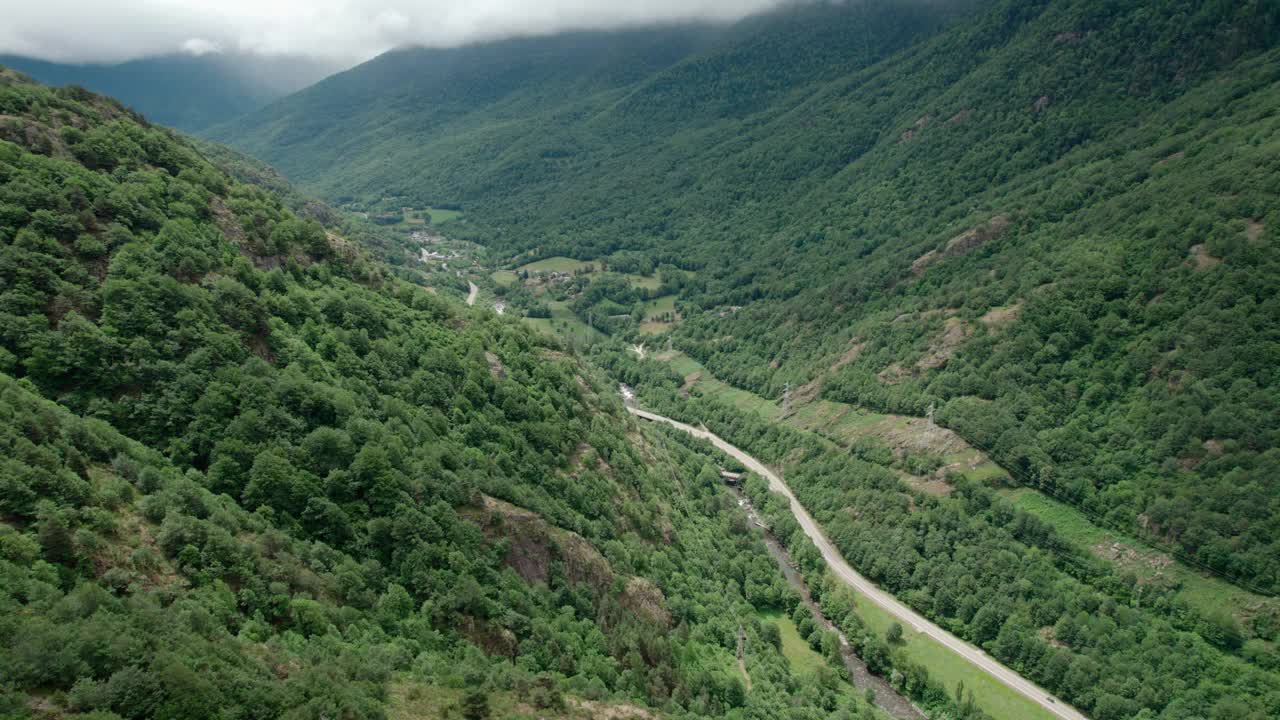 美丽的无人机视野的沥青公路在高山上。山脉消失在天空中，天空有些许阴云，但山峰被阳光照亮。视频素材