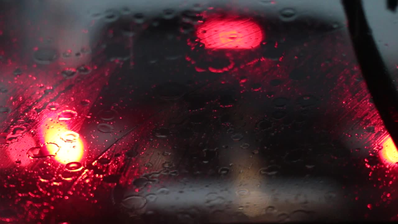 雨落在汽车挡风玻璃上。在暴雨中，驾车行驶在交通堵塞的街道上。视频素材