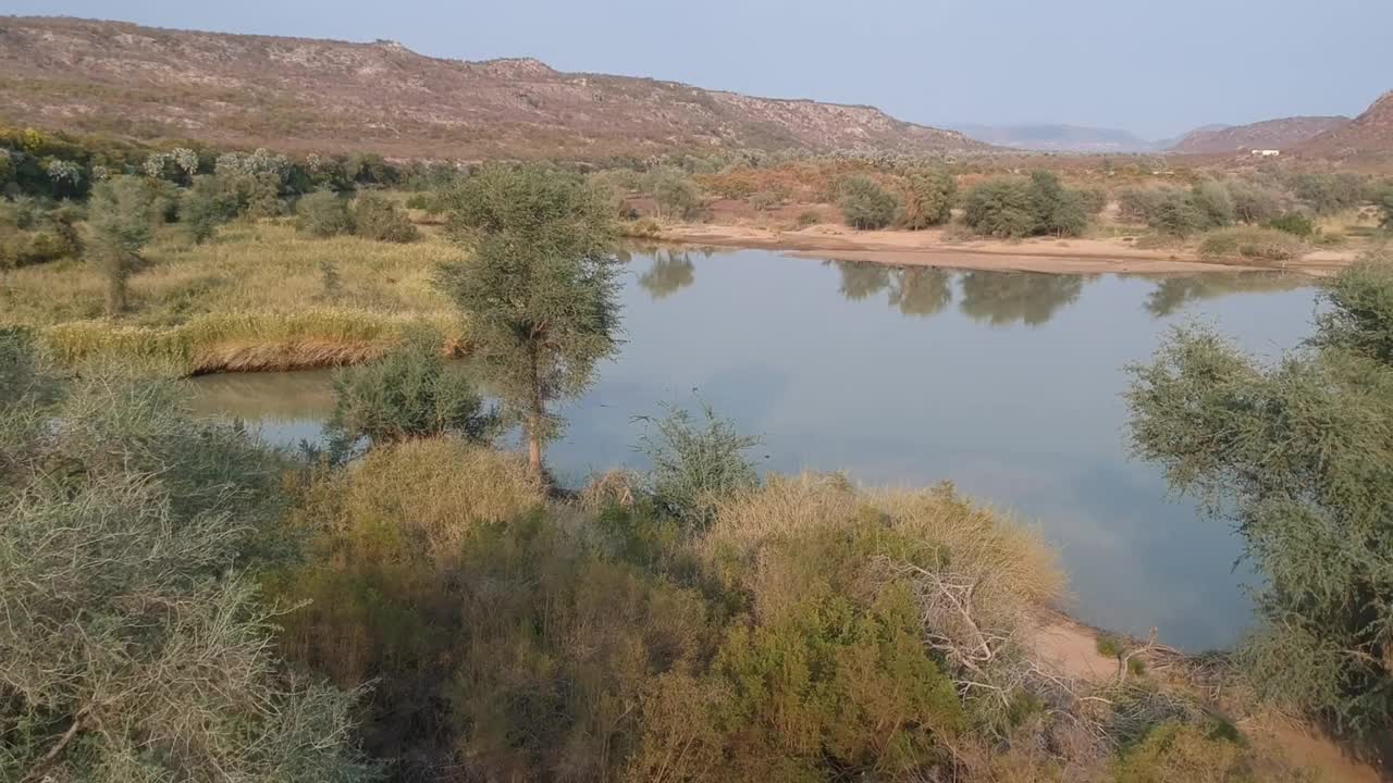 Kunene河的美丽景色与倒影的云和树在水相机上升之间的树向下看河航拍视频视频素材