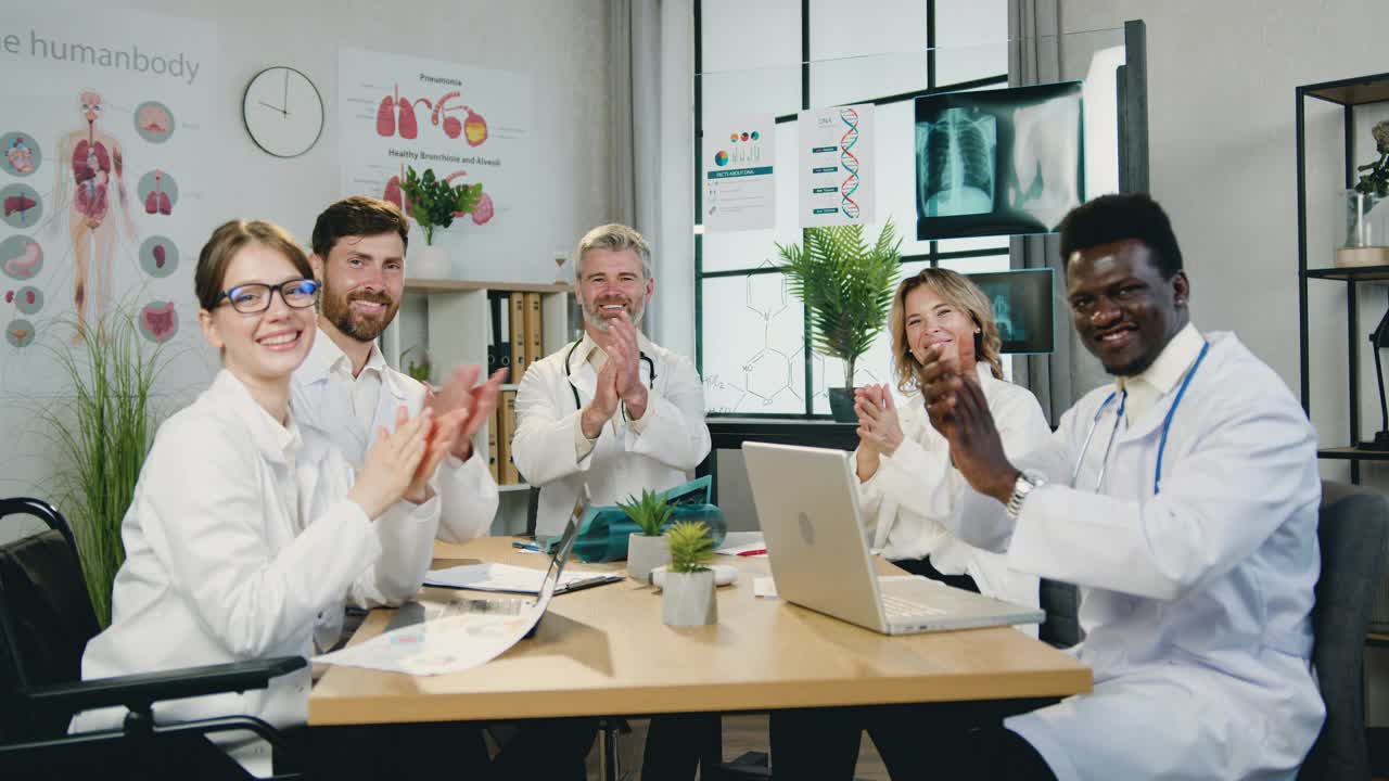 医学概念，有吸引力的快乐微笑合格友好的多元文化的男性和女性医生坐在诊所的工作场所和鼓掌视频素材