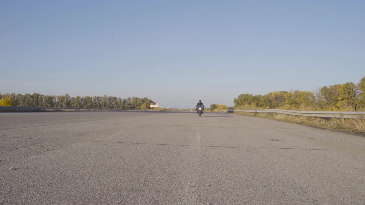 前视图摩托车驾驶在现代运动摩托车在乡村沥青道路上低速。男摩托车手在保护摩托装备缓慢骑他的摩托车通过空的高速公路。视频素材