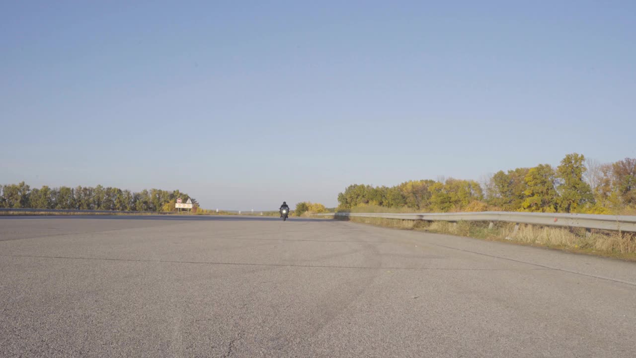 前视图摩托车驾驶在现代运动摩托车在乡村沥青道路上低速。男摩托车手在保护摩托装备缓慢骑他的摩托车通过空的高速公路。视频素材