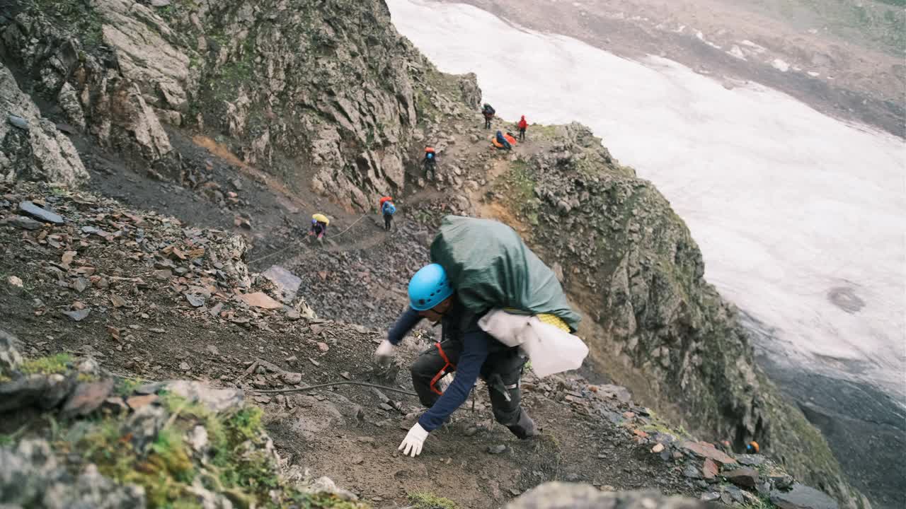 登山者带着一个装有装备的背包爬上了山，背包用系扣固定，系在绳子上的保护绳。视频素材