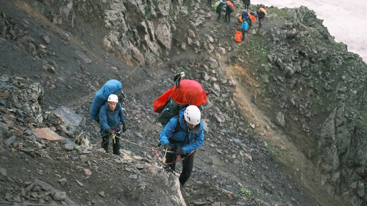 一对扛着大背包的登山者沿着绳索爬到山顶。视频素材