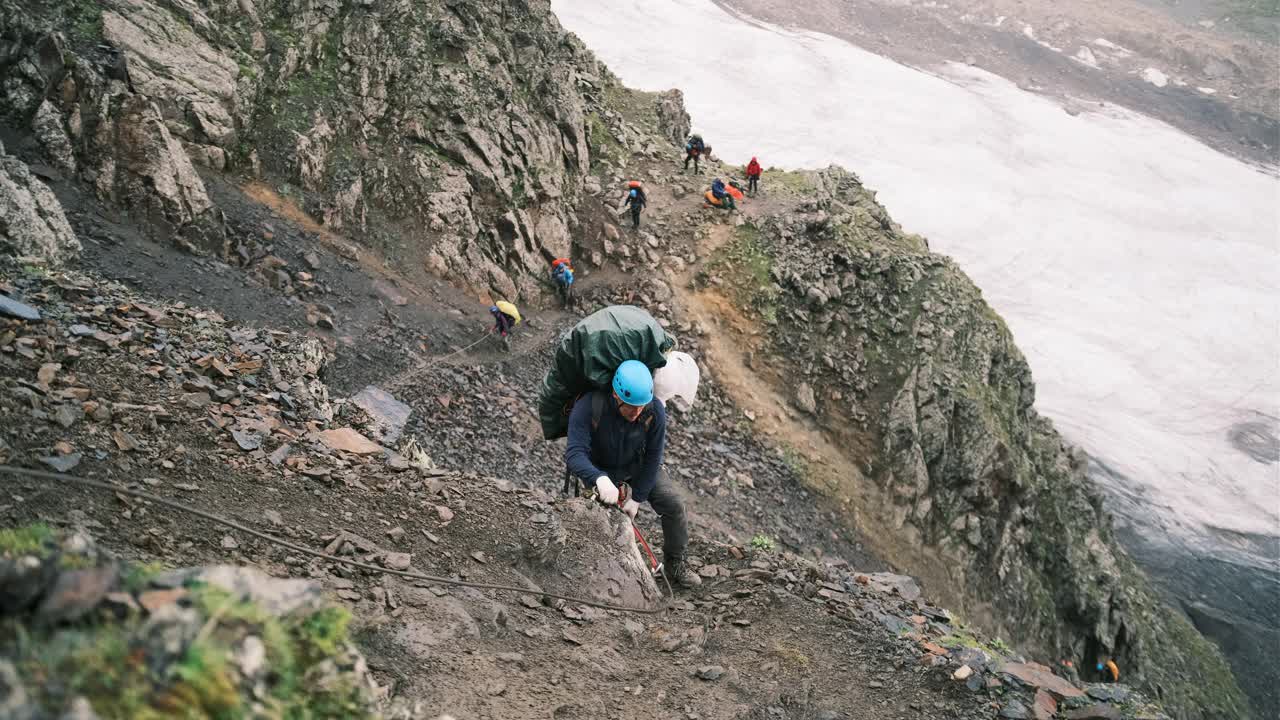 登山者带着一个装有装备的背包爬上了山，背包用系扣固定，系在绳子上的保护绳。视频素材