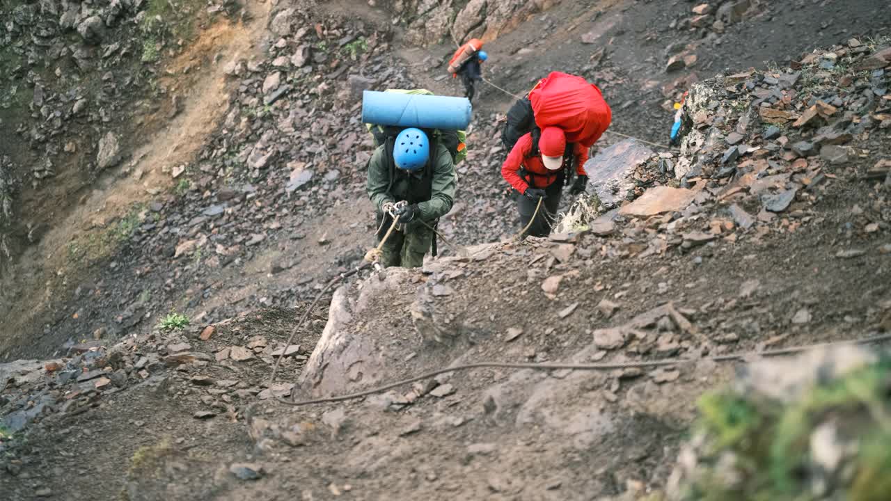 登山者带着一个装有装备的背包爬上了山，背包用系扣固定，系在绳子上的保护绳。视频素材