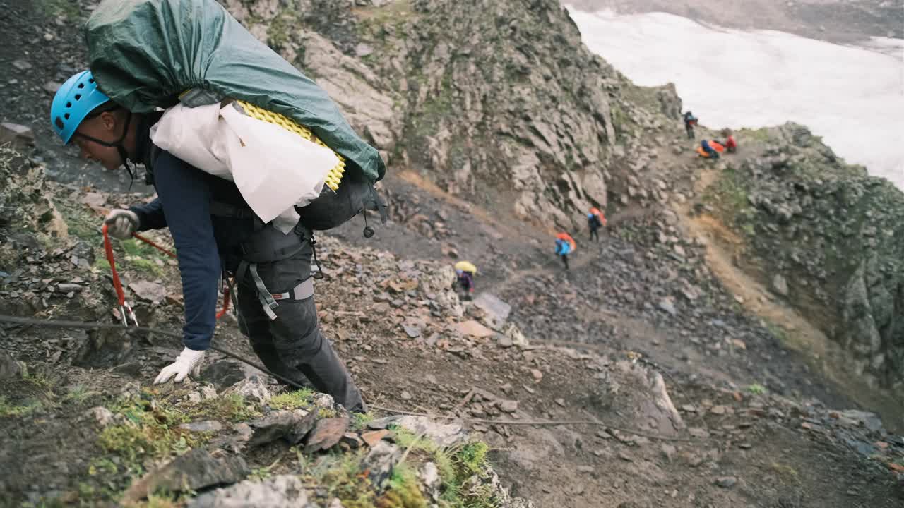 登山者带着一个装有装备的背包爬上了山，背包用系扣固定，系在绳子上的保护绳。视频素材