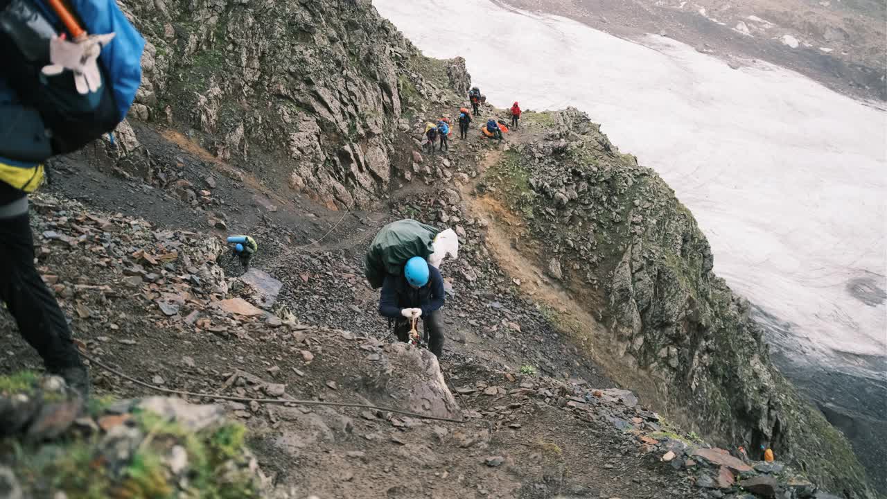 登山者带着一个装有装备的背包爬上了山，背包用系扣固定，系在绳子上的保护绳。视频素材