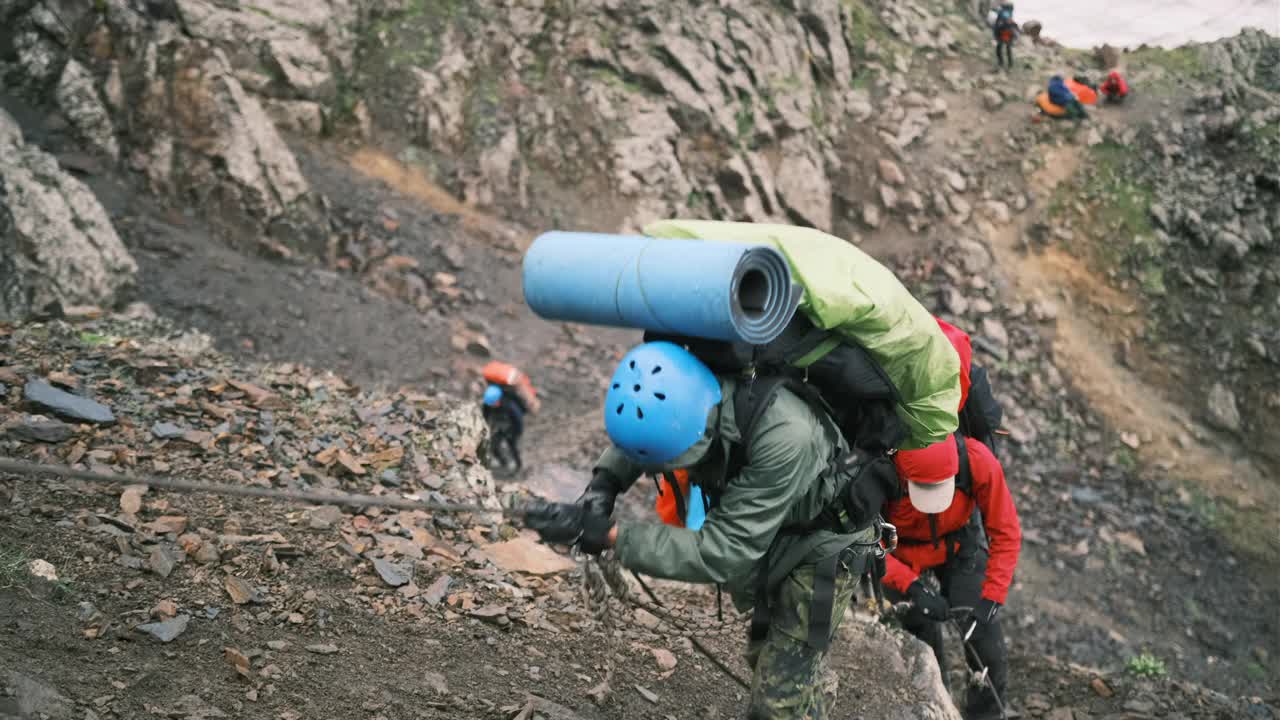 登山者带着一个装有装备的背包爬上了山，背包用系扣固定，系在绳子上的保护绳。视频素材