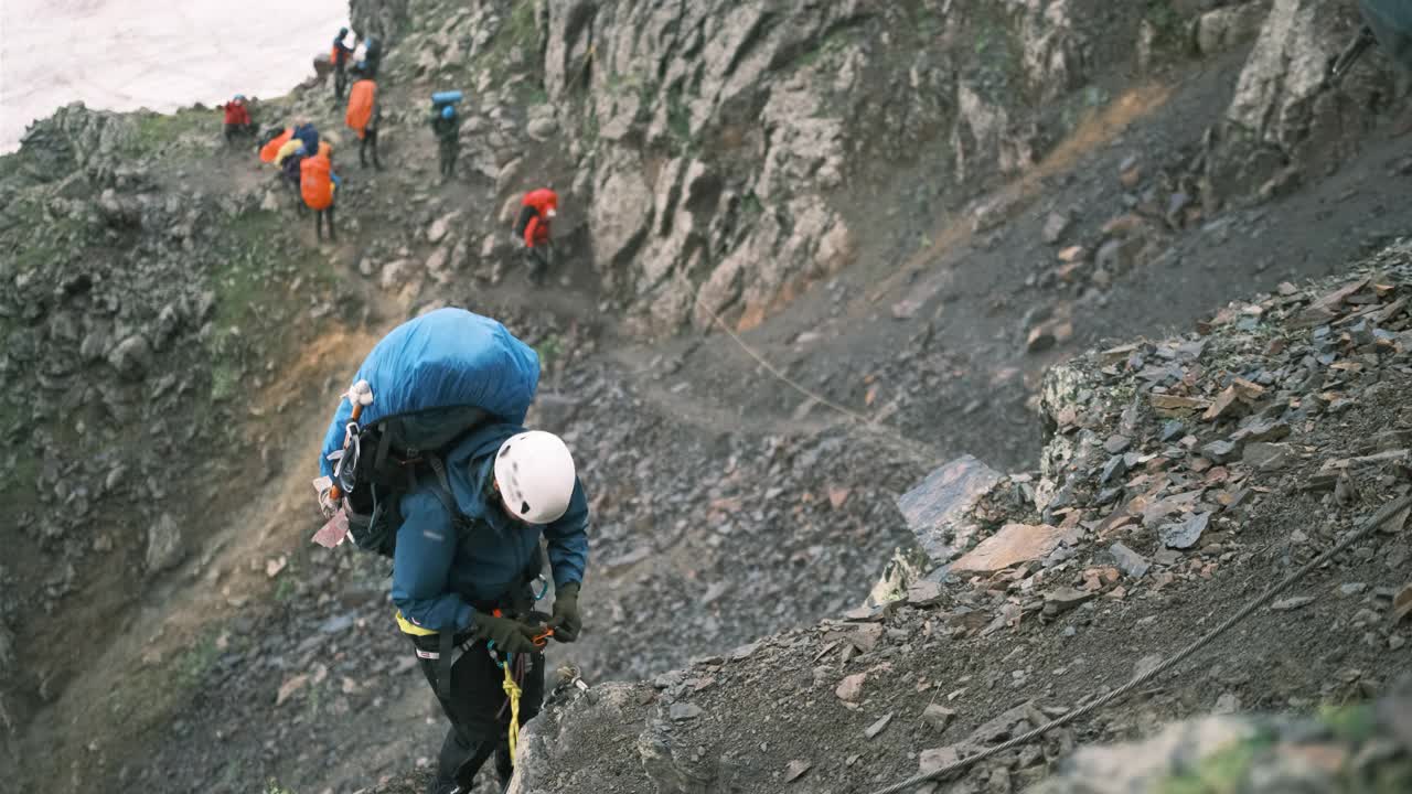 一名登山者背着装备的背包，紧抓钢索爬上了山。视频素材