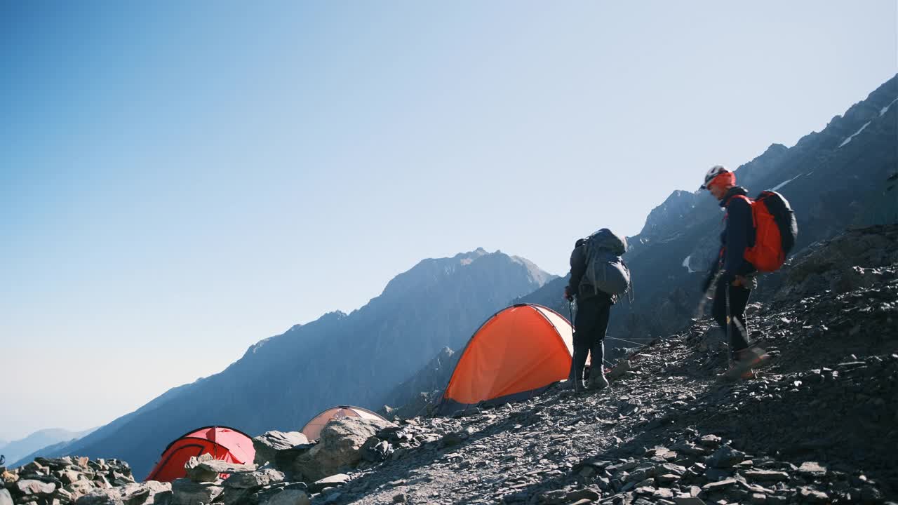 登山队员们爬完山顶，带着帐篷回到营地，卸下沉重的装备背包，喝了一口水解渴视频素材