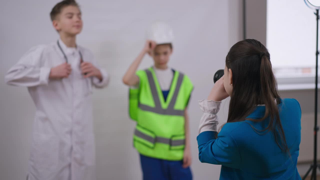 后视图才华横溢的十几岁女孩作为朋友拍照，穿着医生和建筑工人制服，在白色背景下摆姿势。创意自信的白人小摄影师享受室内爱好。视频素材