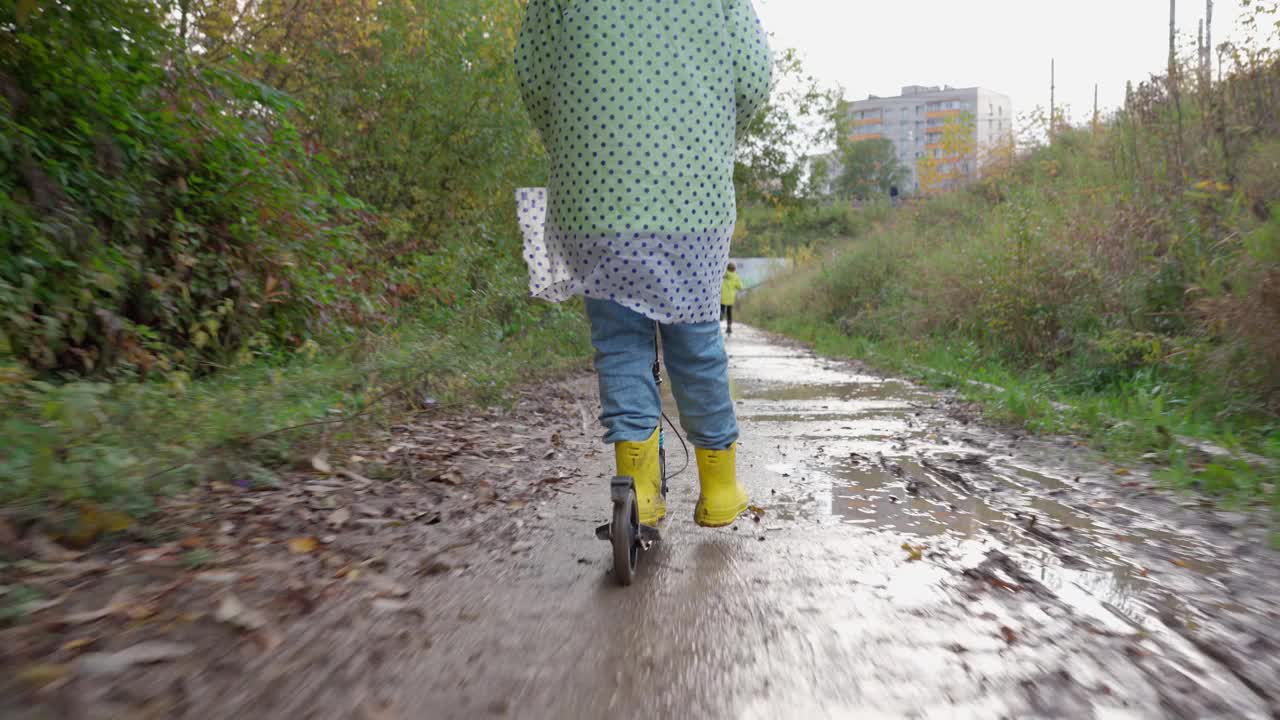 一个穿着雨衣和黄色胶靴的可爱男孩骑着自行车穿过水坑视频素材