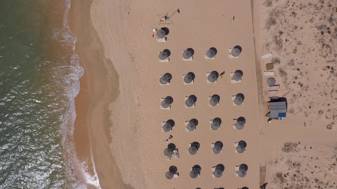 葡萄牙海滨度假胜地的鸟瞰图。阳伞和阳光躺椅从上到下安置在黄色的海滩上。阿尔加夫视频素材