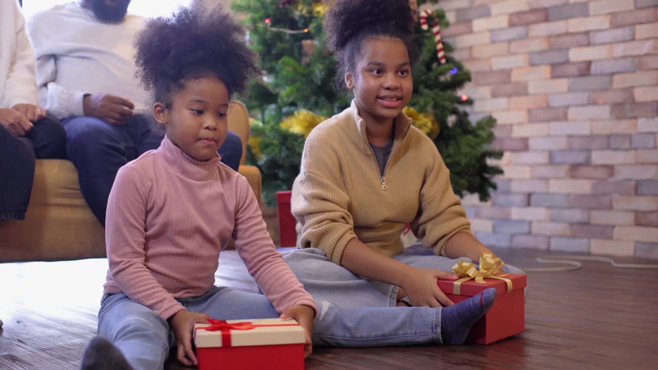 两个女儿在一起享受圣诞节或新年假期时，用礼物盒给她的妈妈和爸爸一个惊喜视频素材