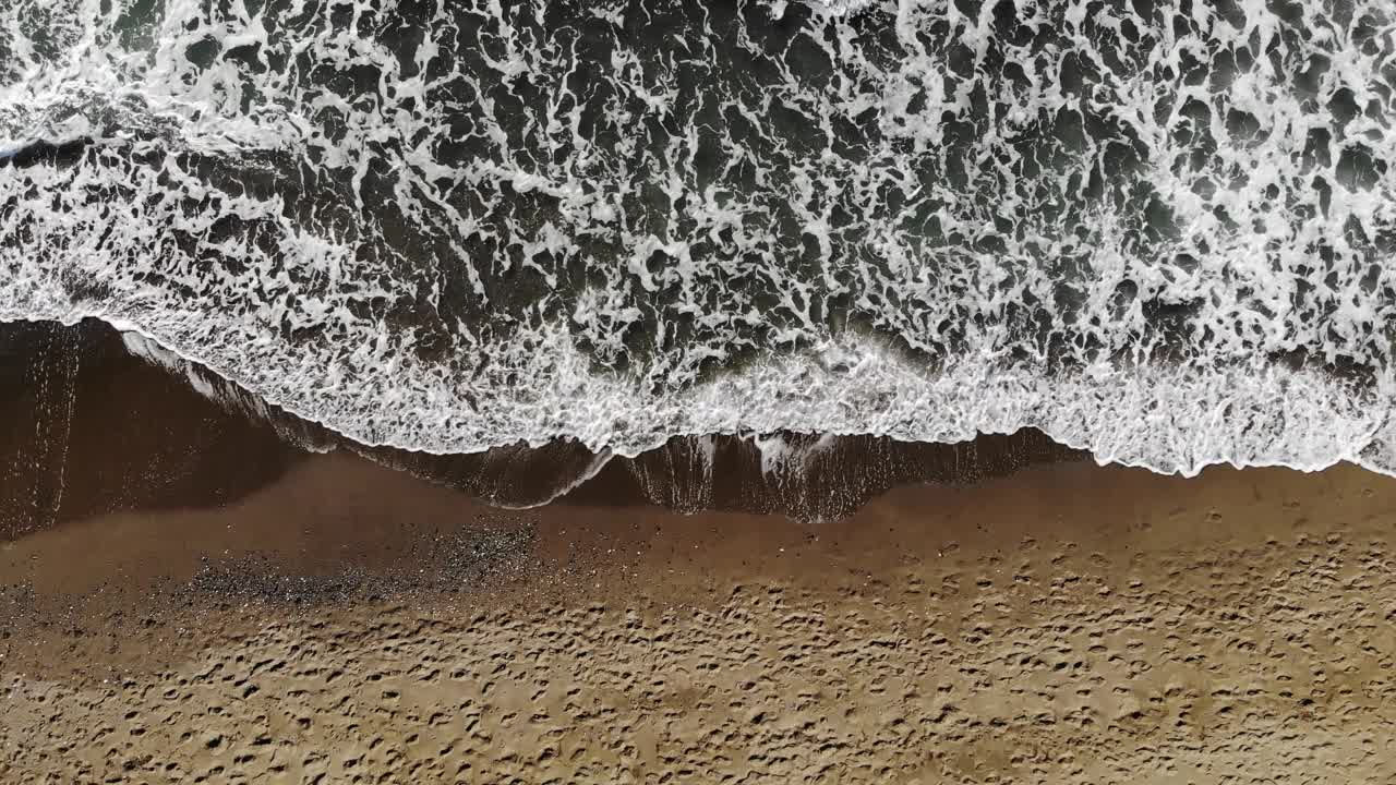 当泡沫般的海浪拍打在沙滩上时，无人机拍摄的无穷无尽的美丽画面。空中拍摄的金色海滩与深海水域相遇。视频下载