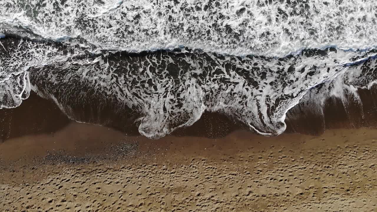 当泡沫的波浪拍打在沙滩上时，无人机拍摄的美丽的无限图像在超慢动作。空中拍摄的金色海滩与深海水域相遇。视频下载