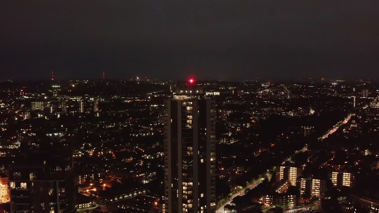 夜间，向前飞在城市附近上空。被窗户和街灯照亮的场景。朝着高大的公寓楼走去。英国伦敦视频素材