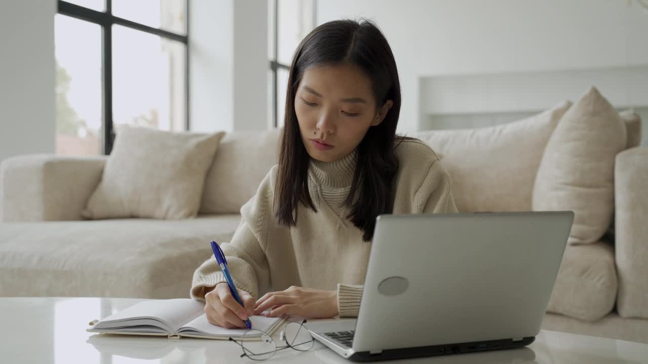 一位年轻的亚洲女学生正在使用电脑和平板电脑。一位年轻的女商人正坐在办公桌前，在笔记本上记着笔记。教育和技术的概念视频素材