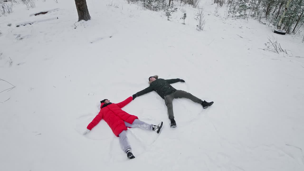 年轻的一家人躺在雪地里。快乐的男人和女人堆雪天使。视频素材