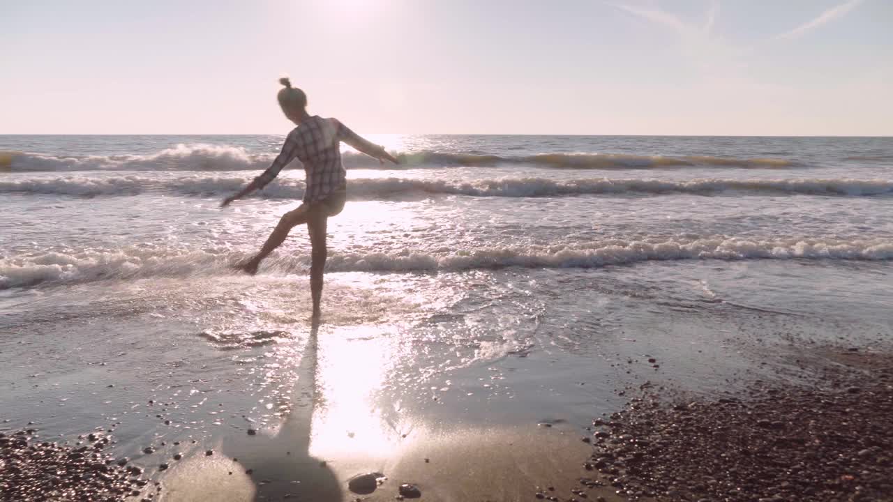 苗条的女人在沙滩上踢海水。飞溅的水视频素材